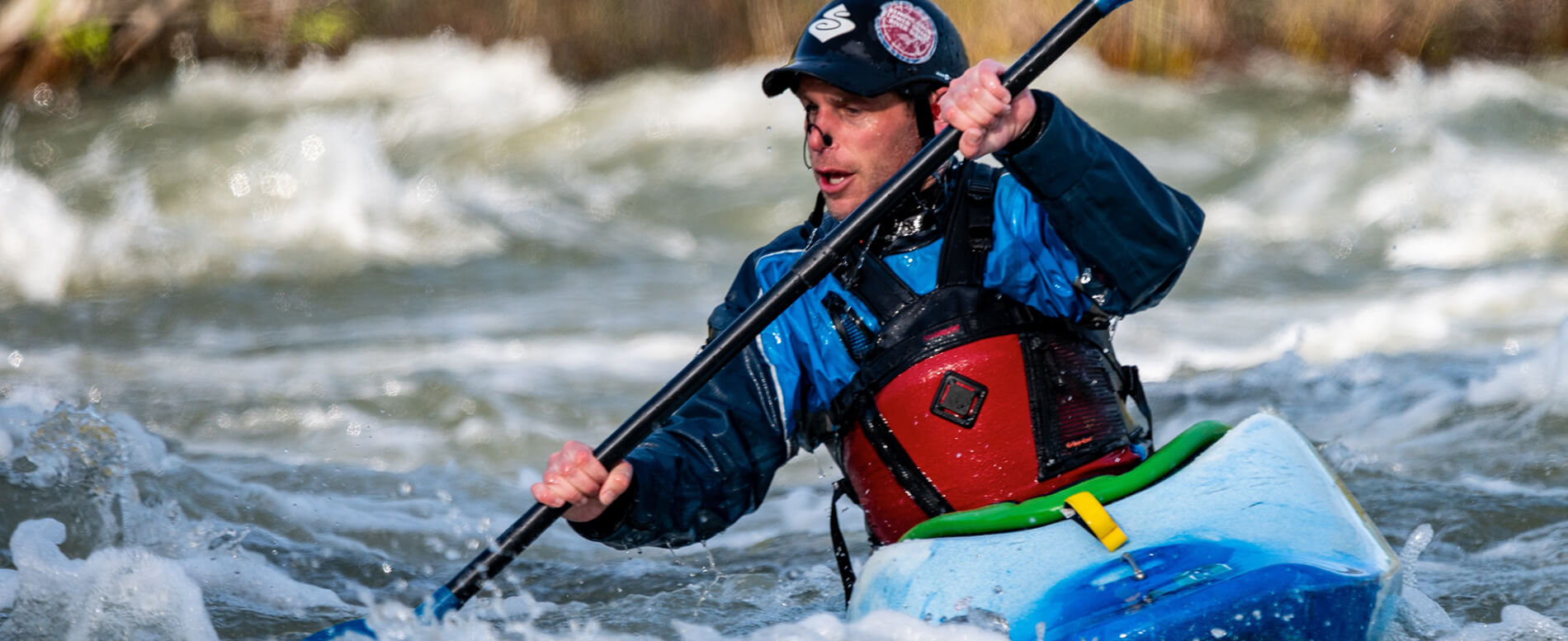 Man on a whitewater kayak wearing a red life jacket