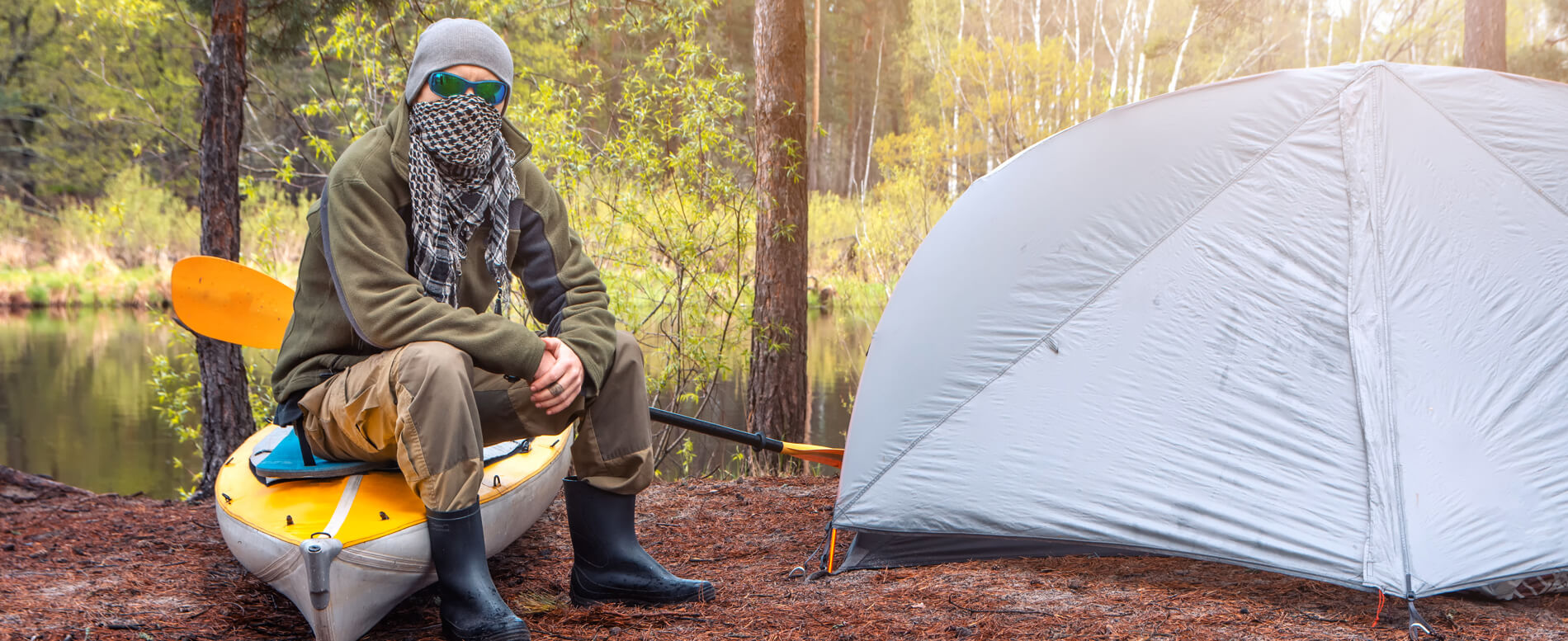 Man sitting on his kayak near a camping tent