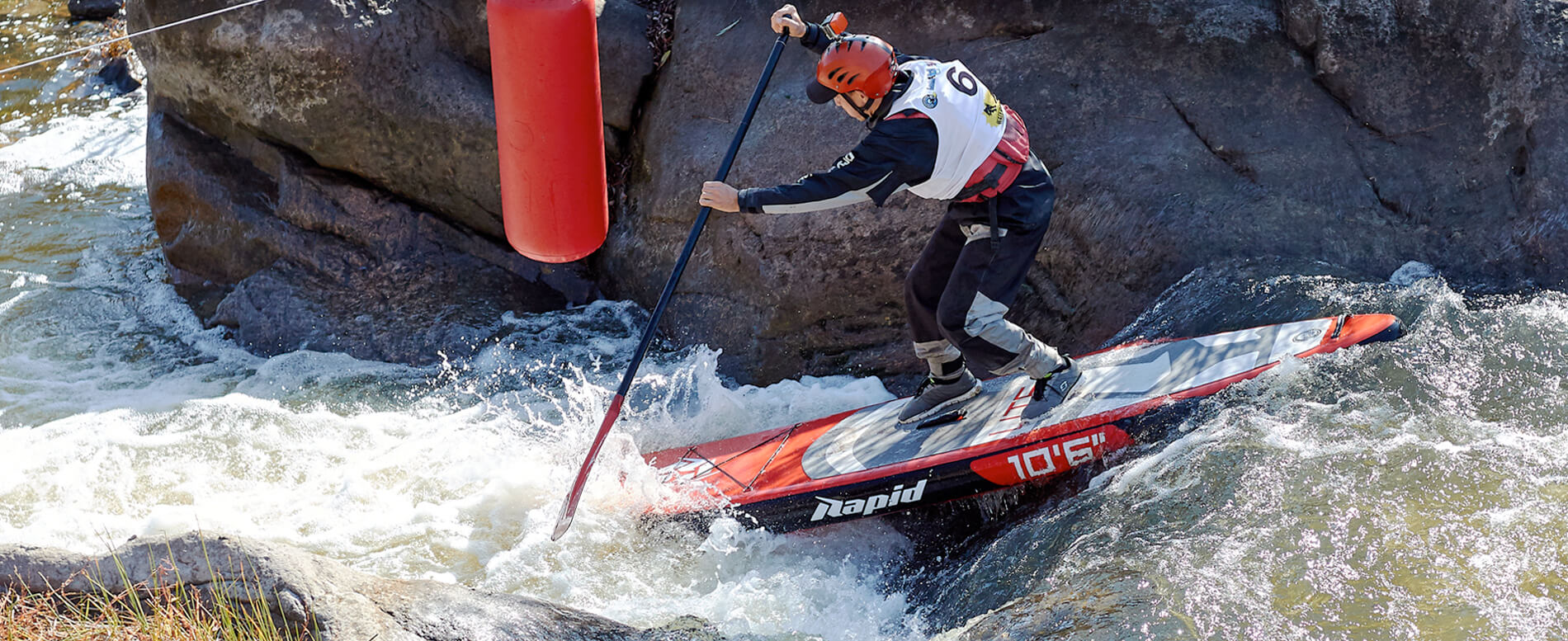 Man paddle boarding on a river near a big rock